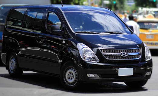 A eight-passenger rental car, a Hyundai Starex, is driving on the road